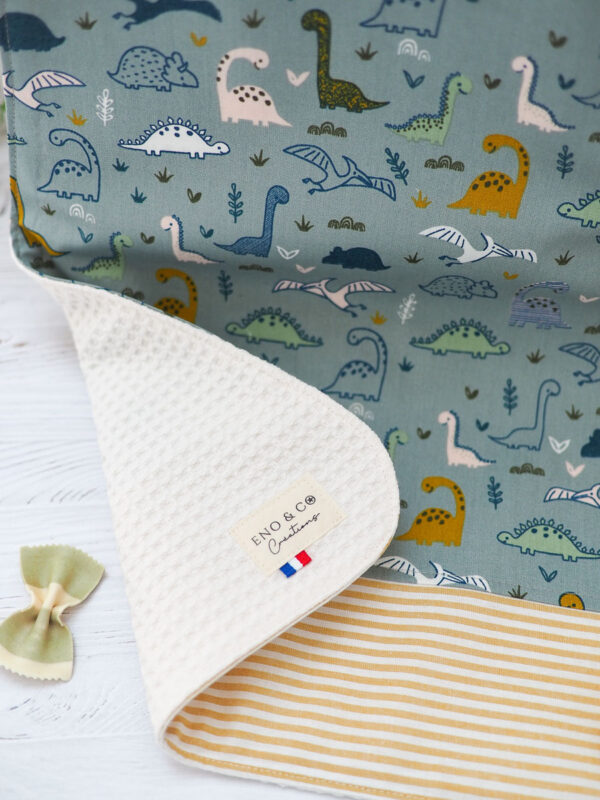Serviette élastique pour enfant "Les Dino" avec motif coloré de dinosaures, taille adaptée aux 2-6 ans, en coton doux et nid d’abeille absorbant.