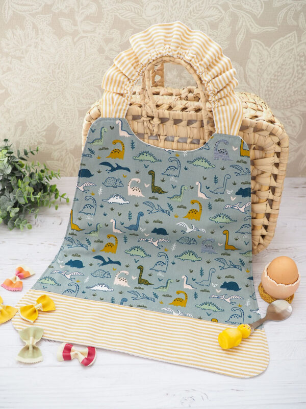 Serviette élastique pour enfant "Les Dino" avec motif coloré de dinosaures, taille adaptée aux 2-6 ans, en coton doux et nid d’abeille absorbant.