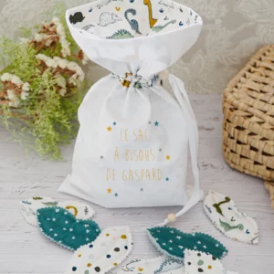 Sac à bisous au motif de dinosaures sur fond beige entouré de ses bisous en tissu aux couleurs assortis